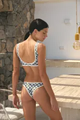 Bikini de dos piezas confeccionado en lycra brillante con estampado geométrico de monograma. El corpiño presenta un diseño de escote redondo con breteles anchos y ribetes en contraste color perla. La bombacha es de corte vedetina con los mismos ribetes en contraste.