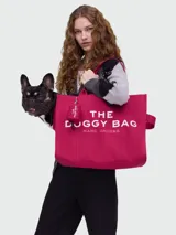 Bolso tote color fucsia, modelo The Doggy Bag, con texto estampado en blanco que dice "THE DOGGY BAG MARC JACOBS". Presenta un diseño acolchado vertical y asas de mano.