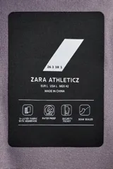Cazadora deportiva de esquí con diseño bicolor en tonos negro y verde oliva. Presenta capucha amplia con visera, cierre frontal con cremallera termosellada, bolsillos frontales y en manga con cierres impermeables, y aberturas de ventilación en las axilas. Incluye faldón interior antinieve, puños ajustables y tecnología de rescate RECCO.