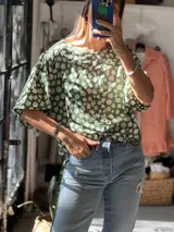 Blusa de corte holgado con estampado floral en tonos verde y blanco. Presenta cuello redondo tipo bebé, mangas cortas abullonadas y cierre frontal con botones ocultos.