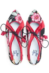 Zapatos tipo blucher de diseño artesanal, confeccionados en algodón con estampado floral multicolor sobre base negra. Presentan detalles en terciopelo color fresa, cierre con cordones rematados en borlas y suela de cuero.