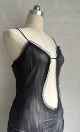 Vestido corto ajustado color negro con estampado a cuadros difuminado. Presenta escote pronunciado con abertura central y bordes de encaje negro. Tiene tirantes finos y frunces en la falda.