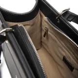 Cartera estructurada mediana de material símil cuero negro, con doble manija fija y correa larga regulable y desmontable. Presenta solapa frontal con botón imantado y herrajes metálicos plateados.