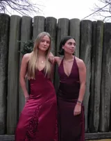 Vestido largo sin mangas con escote en V halter y aberturas laterales (cut-outs) en la cintura. El cuerpo superior presenta un llamativo diseño estampado multicolor, mientras que la falda larga es de tejido texturizado brillante en color verde esmeralda con inserciones godet en el ruedo.