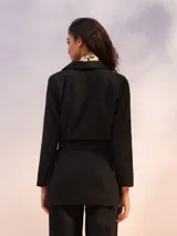 Blazer negro de corte recto con solapas anchas y lazo ajustable en la cintura.