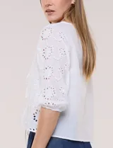 Cardigan corto de broderie blanco con escote en V y cierre frontal de lazos para anudar. Presenta mangas tres cuartos abullonadas con puño elástico y diseño perforado con motivos florales.