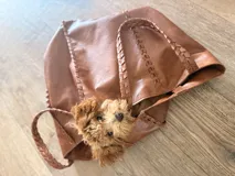 Bolso tipo tote de cuero color marrón, con diseño artesanal que presenta detalles de costuras trenzadas en los laterales y en el centro. Cuenta con dos asas superiores trenzadas y un tamaño amplio.