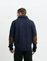 Cardigan de punto color marrón con cuello esmoquin, cierre frontal con botones y presilla superior. Presenta mangas largas con coderas en contraste y bolsillos frontales de ribete.