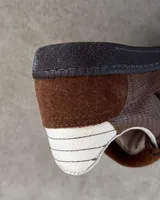 Championes de cuero vacuno con diseño de paneles en tonos marrones y detalles en blanco. Presentan una combinación de texturas lisas y grabadas, con cordones planos y costuras decorativas en la lengüeta.