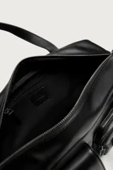 Bolso bandolera negro de acabado liso, con compartimento principal con cierre de cremallera. Cuenta con dos bolsillos frontales, uno con solapa y detalle metálico y otro con cremallera. Incluye dos asas de mano y un asa de hombro ajustable y extraíble, además de detalles de charms y mosquetón en un lateral.