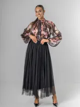 Camisa de seda italiana con estampado floral en tonos rosados, marrones y verdes. Presenta cuello alto con volados que caen en cascada sobre el frente y mangas largas abullonadas con puños ajustados.