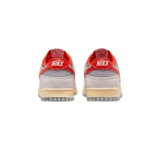 Championes Nike Dunk Low con diseño de paneles en tonos gris claro y blanco, destacando el swoosh lateral y detalles en el talón y cuello en color rojo vibrante. Presenta cordones en tono crema y una suela con efecto envejecido.