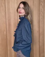 Camisa de manga larga con estampado de cuadros en tonos marrones y azules. Presenta cuello alto con volados, cierre frontal con botones y puños con volados.