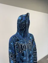 Buzo tipo hoodie tejido de punto grueso con cierre frontal completo hasta la capucha. Presenta un diseño gráfico abstracto en tonos azules y negros, con tipografía estilo gótico en el frente y las mangas. Cuenta con puños y ruedo acanalados en color negro, y etiqueta de marca en la manga.