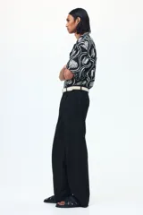 Pantalón sastrero de sarga en color negro, con corte holgado, piernas amplias con raya marcada, cierre frontal con botón y corchete ocultos, bolsillos al bies y bolsillos traseros insertados.
