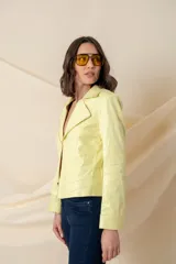 Chaqueta de cuero ecológico color vainilla, con cuello clásico, cierre frontal descentrado con cremallera metálica dorada y pespuntes decorativos.