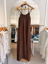 Vestido largo marrón de silueta amplia y caída fluida, confeccionado en mezcla de modal y poliéster. Presenta escote fruncido con tirantes finos que se atan al cuello y espalda con elástico.