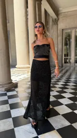 Falda larga negra de tejido red calada con lurex dorado, pretina elástica y tajos laterales. Incluye forro en la zona del caderín.