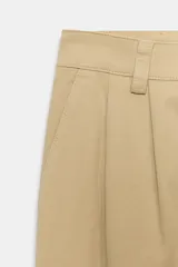 Pantalón chino de tiro medio, corte recto y holgado, con pinzas en la parte delantera. Presenta bolsillos laterales, falsos bolsillos traseros con solapa y bajo con dobladillo vuelto. Cierre frontal con cremallera y botones.