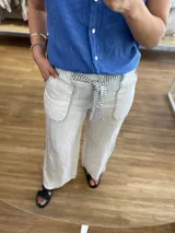 Pantalón de lino línea italiana, color blanco, de corte recto y holgado. Cuenta con bolsillos delanteros redondeados con ribete de rayas y un lazo ajustable en la cintura.