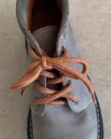 Borcego de cuero color gris con cordones color naranja, suela track negra de goma y detalle de gamuza en la parte superior del tobillo.