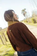 Chaqueta corta de gamuza marrón, con amplio cuello smoking y solapas de corderito en color mostaza, diseño cruzado con doble abotonadura, mangas amplias y bolsillos exteriores.