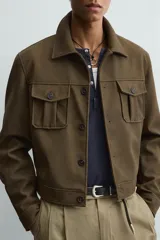 Cazadora cropped fit de efecto piel en color verde militar, con cuello solapa, manga larga con puño abotonado, bolsillos frontales de plastrón con solapa y cierre de botonadura.