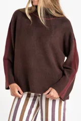 Polera de punto con calce oversize, cuello alto y mangas largas. Presenta un diseño en color negro con franjas laterales en las mangas y detalle en el cuello en tono bronce con acabado brillante.