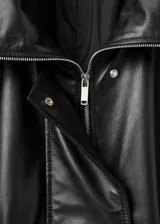 Parka oversize de cuero de piel de ovino color negro, con cuello embudo, solapas amplias y cierre oculto de cremallera y botones. Cuenta con manga larga con puños elásticos y dos bolsillos laterales.