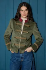 Blazer corto de estilo militar confeccionado en terciopelo azul marino, con cuello mao, cierre frontal con cremallera, detalles de galones bordados y botones metálicos decorativos.