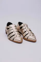 Sandalias bajas de cuero color dorado con tiras entrecruzadas y hebillas ajustables. Taco de madera.