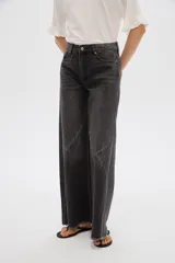 Pantalón jean gris de tiro alto, corte ancho (wide leg) con diseño de paneles tipo patchwork y terminación desmechada en el dobladillo.
