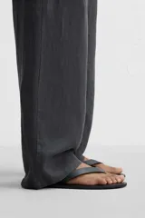 Sandalia minimalista de cuero negro, con tira delgada en el empeine y suela plana.