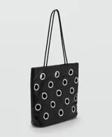 Bolso tipo shopper de color negro con diseño de ojales metálicos plateados. Cuenta con doble asa de hombro y cierre de botón magnético.