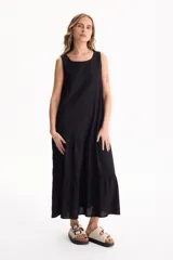 Vestido largo negro de lino, sin mangas, con escote redondo y diseño fluido con volados escalonados en la falda.