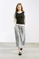 Falda midi de tiro medio, color gris claro con estampado de lunares negros. Presenta cintura ajustable con lazada y bolsillos laterales ocultos.