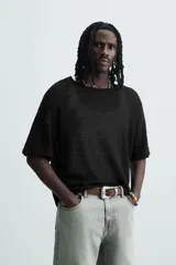 Camiseta de punto negro, corte relajado, con cuello redondo amplio y manga corta. El tejido es ligero y calado.