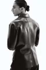 Camisa de manga larga color verde oscuro con acabado brillante (efecto charol o vinilo), cuello clásico y botones forrados al frente. Presenta costuras visibles que definen paneles y un bajo redondeado.