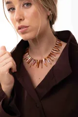 Collar corto tipo gargantilla compuesto por bastones de nácar teñidos en tonos cobrizos y mostacillas. Cuenta con cadena de acero quirúrgico para regular el largo.