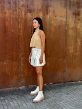 Falda corta tipo wrap de cuero color crudo, con diseño cruzado y ajuste mediante tiritas laterales.