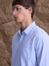 Camisa de manga larga con estampado de rayas verticales finas en color azul y blanco. Presenta cuello clásico, cierre frontal con botones y un bolsillo en el pecho.