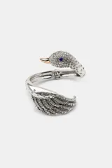 Brazalete tipo esclava plateado con forma de cisne. La cabeza del cisne está cubierta de pequeñas piedras de cristal transparentes, con un ojo de cristal azul y el pico dorado. El cuerpo del cisne simula alas con capas de piedras de cristal.
