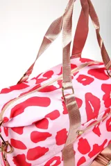 Bolso tipo duffel con estampado animal print en tonos crema y negro. Cuenta con correas de mano y correa ajustable para el hombro en color negro, cierre principal superior y bolsillo frontal con cierre.