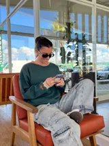 Buzo verde oscuro de algodón, con cuello redondo y puños acanalados con borde naranja.