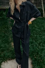 Chaqueta de estilo safari confeccionada en mezcla de lino, color azul marino, con cuello solapa, mangas cortas y cierre frontal con botones ocultos. Presenta bolsillos de parche en el pecho con solapa y botones, además de un cinturón ajustable del mismo tejido para anudar en la cintura.