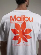Remera blanca de algodón con estampado trasero en color naranja que incluye la palabra "Malibu", una hoja de palma y texto adicional.
