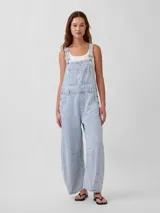 Mono enterito de denim celeste con diseño de rayas verticales blancas, corte holgado tipo horseshoe, tirantes ajustables y bolsillos frontales.