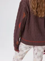 Sweater de punto con diseño de ochos en color verde, cuello redondo con detalle de franja en contraste, y apliques de rombos en las mangas. Presenta un bordado con la letra M en el pecho.