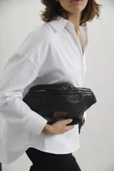 Riñonera de cuero negro con cierre superior y etiqueta de marca Nubia en color marrón.