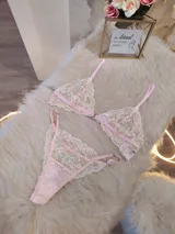Conjunto de lencería compuesto por un bralette y una tanga, confeccionados en encaje bitono rosa y champagne con diseño floral. El bralette presenta cierre frontal con broche de gancho y breteles regulables. La tanga es de estilo colaless con laterales regulables.